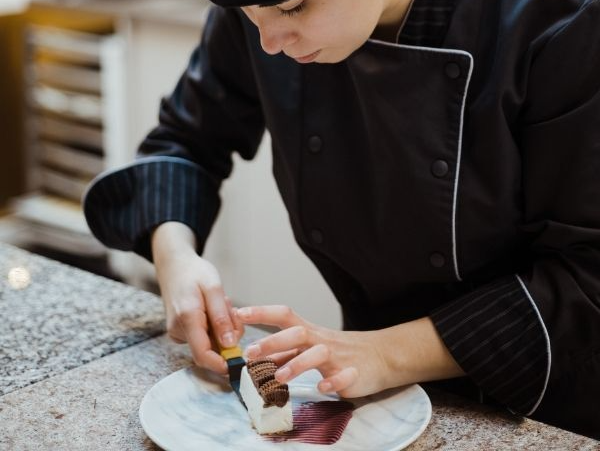 Eine Frau in einer Kochuniform dekoriert einen Teller mit Pralinen