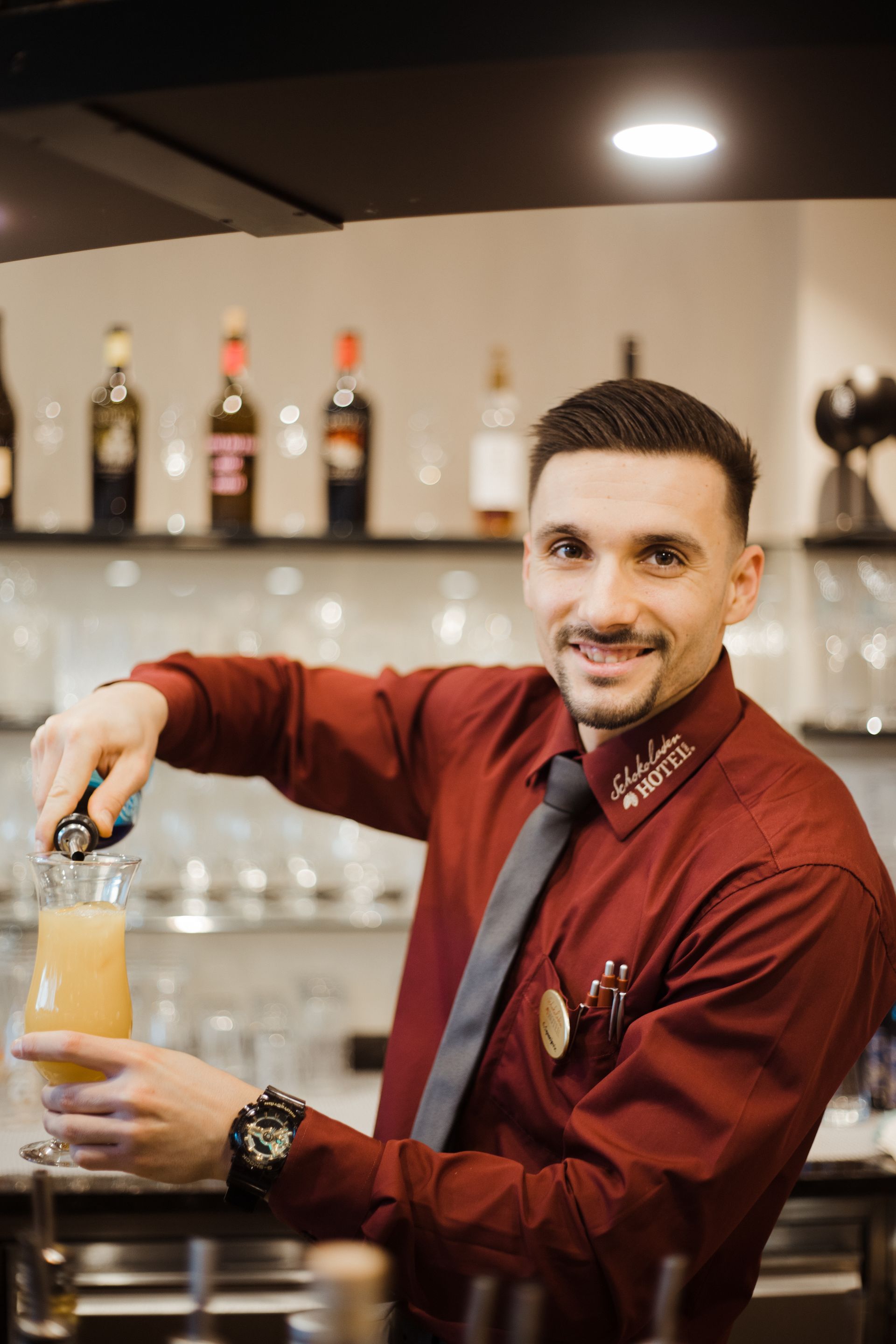 Ein Mann in rotem Hemd und Krawatte gießt einen Drink in ein Glas.