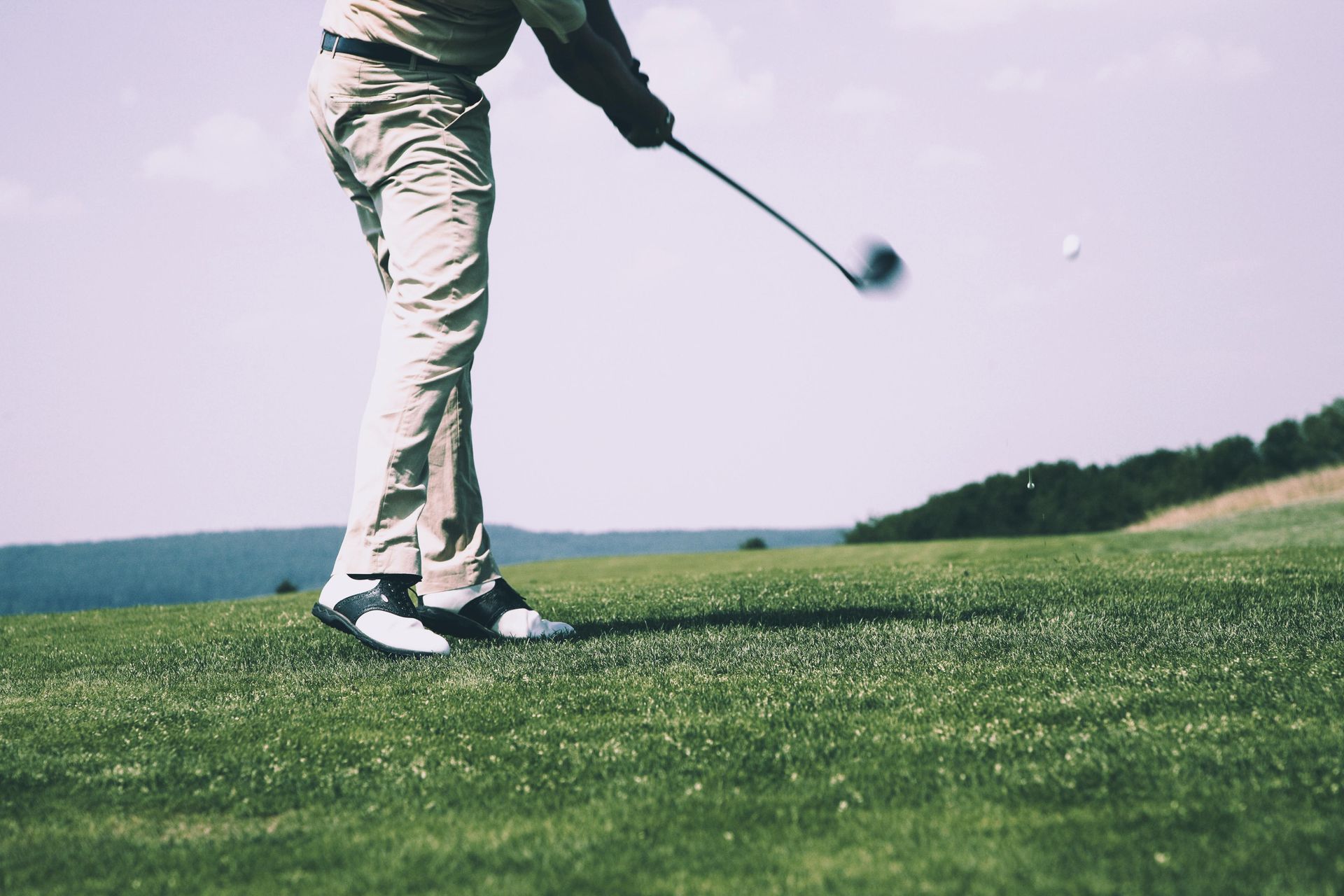 Ein Mann schwingt auf einem Golfplatz einen Golfschläger nach einem Golfball.