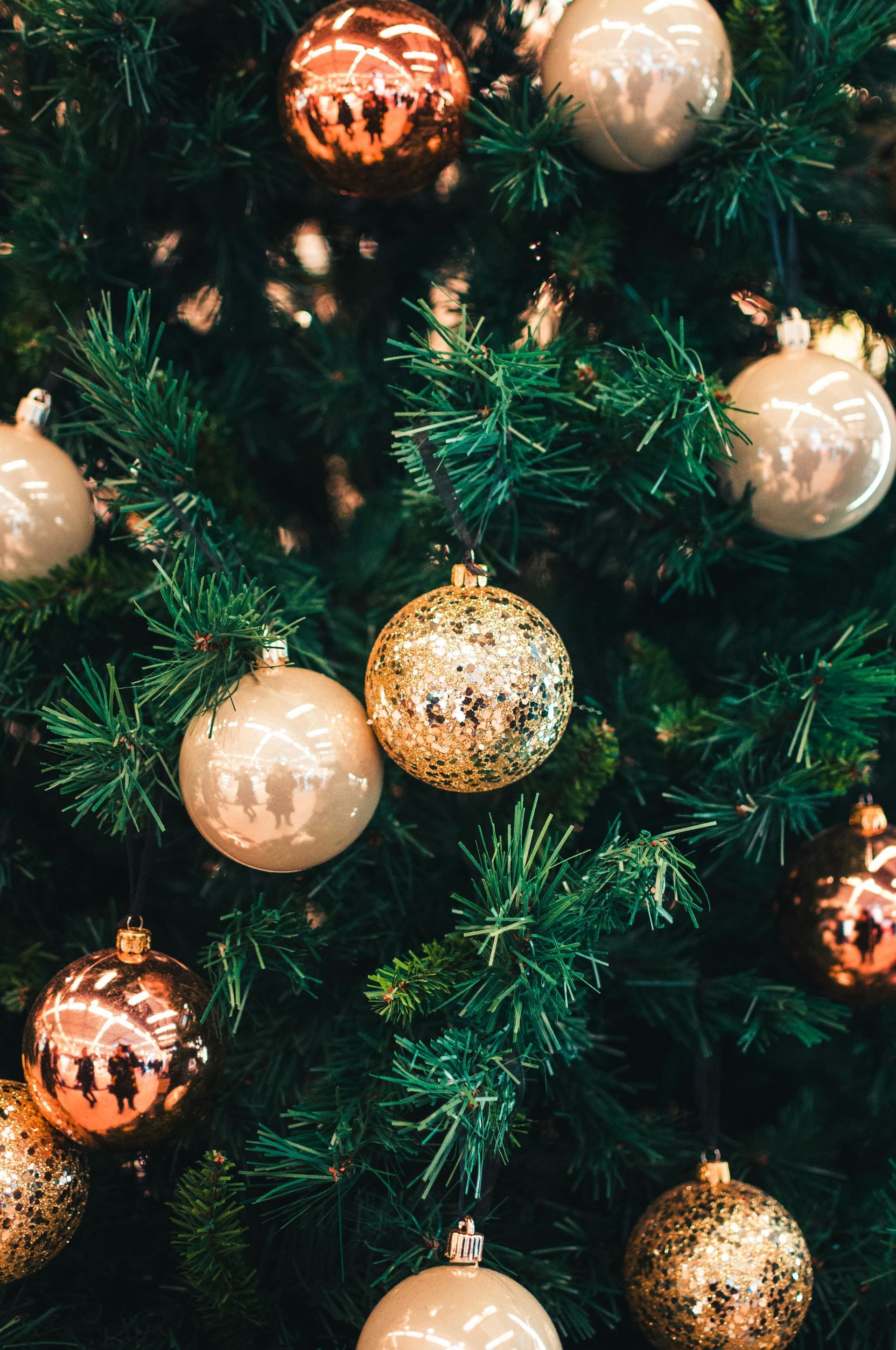 Nahaufnahme eines geschmückten Weihnachtsbaums. Der Schmuck ist gold-, silber- und roségoldfarben.
