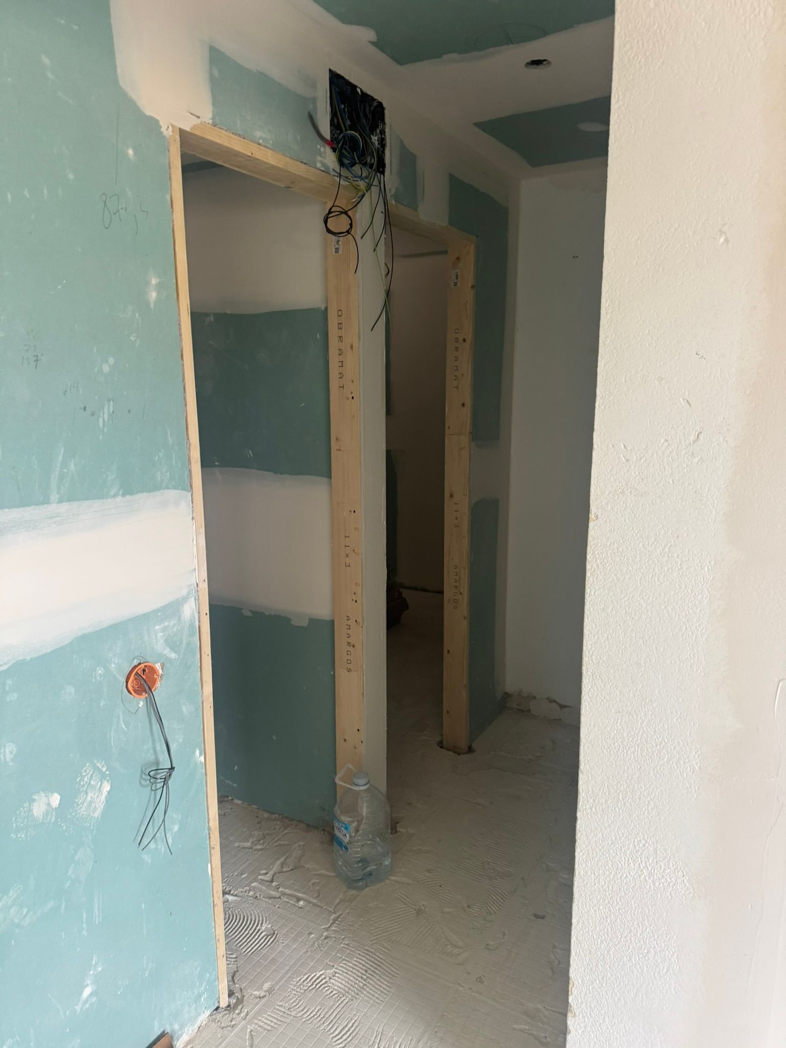 Pasillo sin terminar con pintura descascarada, marco de puerta a la vista y polvo de construcción en el suelo.