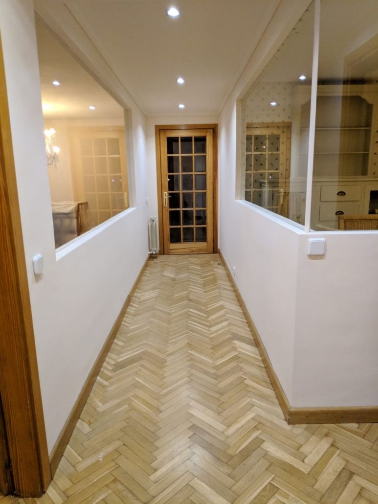 Un largo pasillo con suelo de espiga y una puerta de cristal.