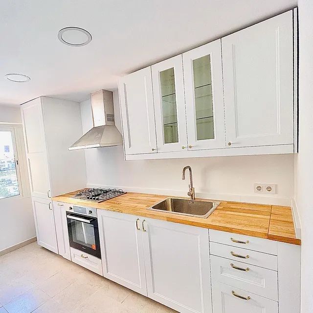 Una cocina con gabinetes blancos y encimera de madera.
