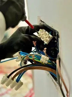 Una persona está trabajando en una toma de corriente eléctrica con un destornillador.