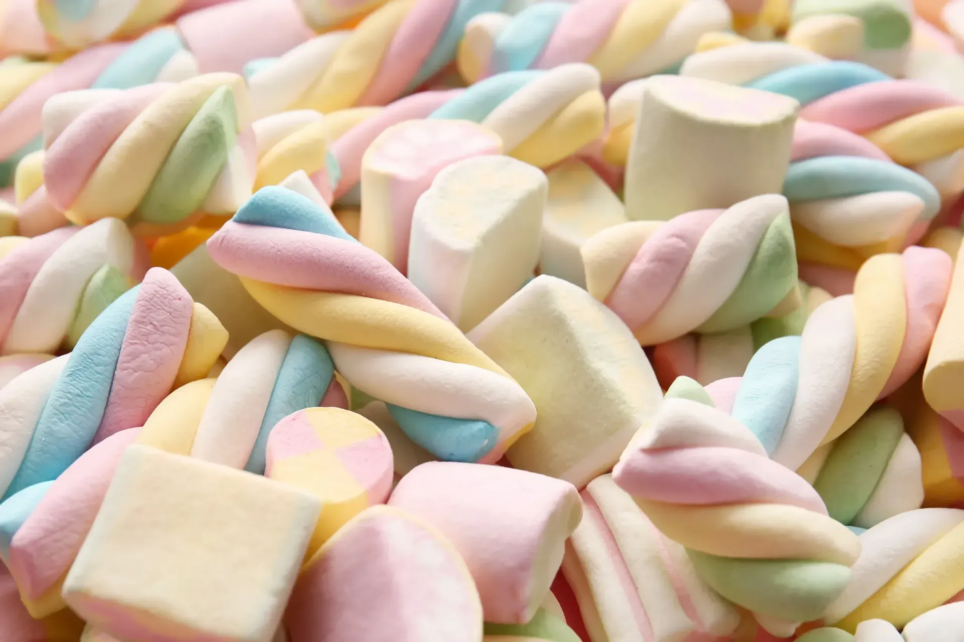 Malvaviscos coloridos, retorcidos y cilíndricos, en tonos rosa pastel, azul, amarillo y blanco.
