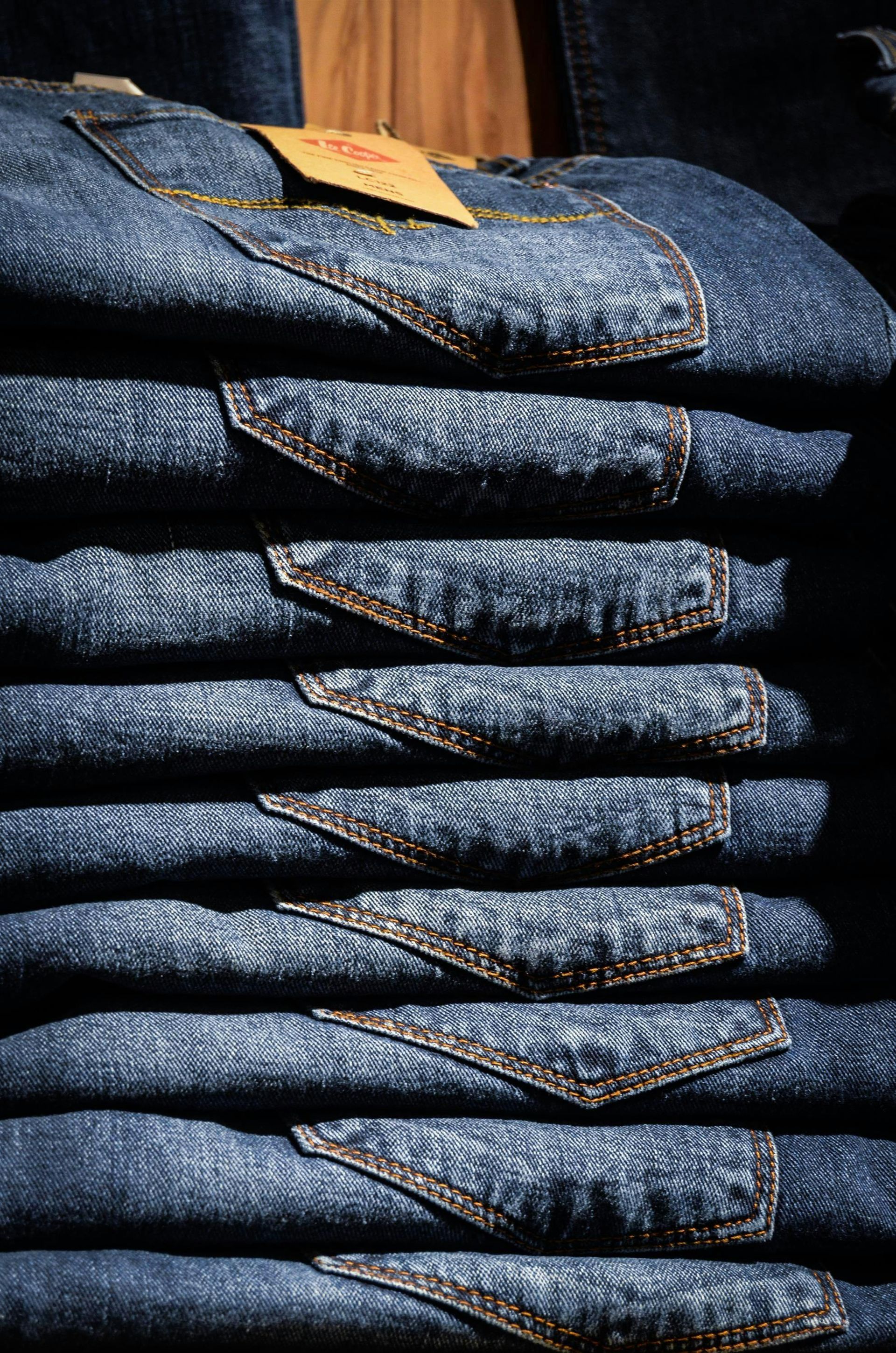 Pila de jeans azules doblados, con bolsillos traseros visibles y una etiqueta de la tienda en la parte superior.
