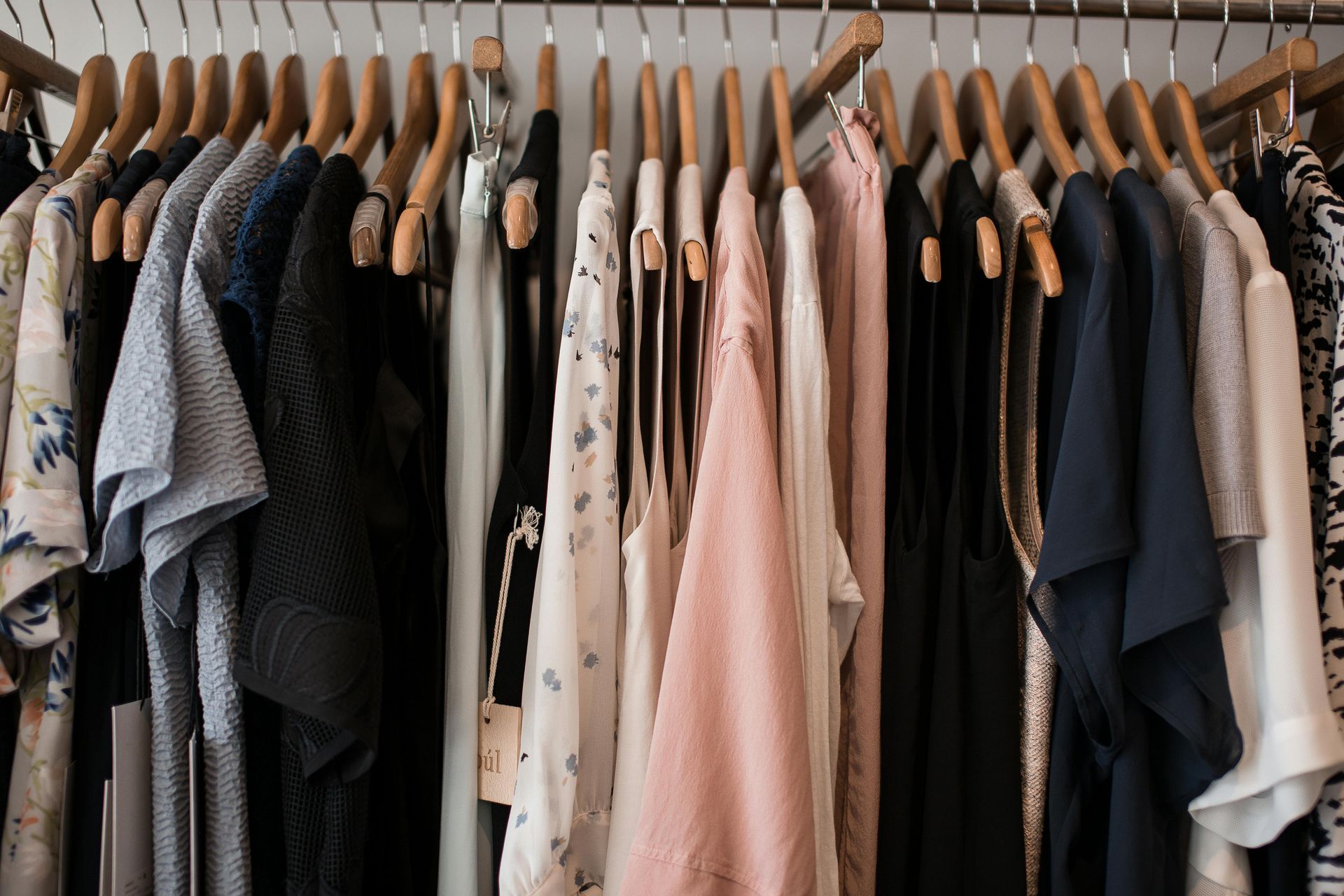 Ropa colgada en perchas de madera en un armario; una mezcla de colores que incluye negro, blanco y rosa.