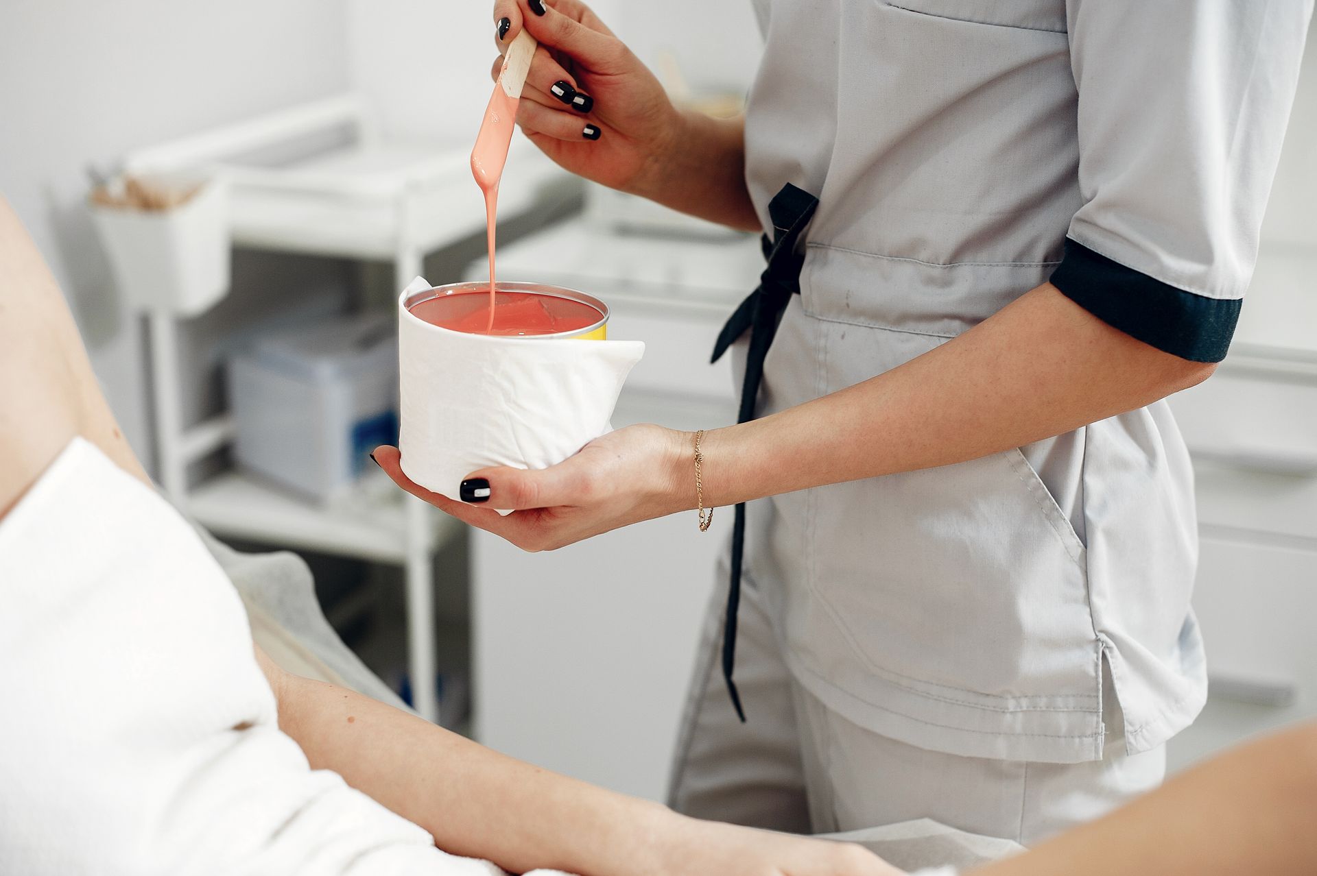 Une aide-soignante remue de la cire dans un bol à côté d'un client alité dans un spa.