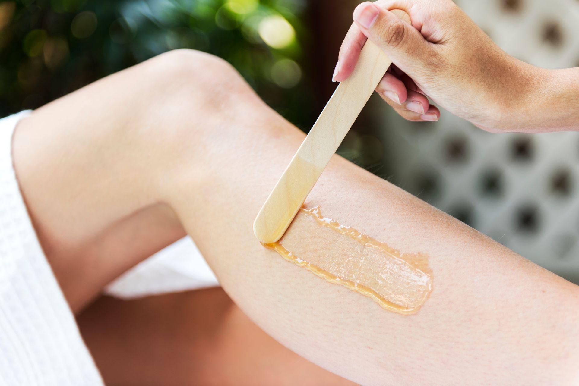 Application de cire sur une jambe à l'aide d'une spatule en bois pour l'épilation