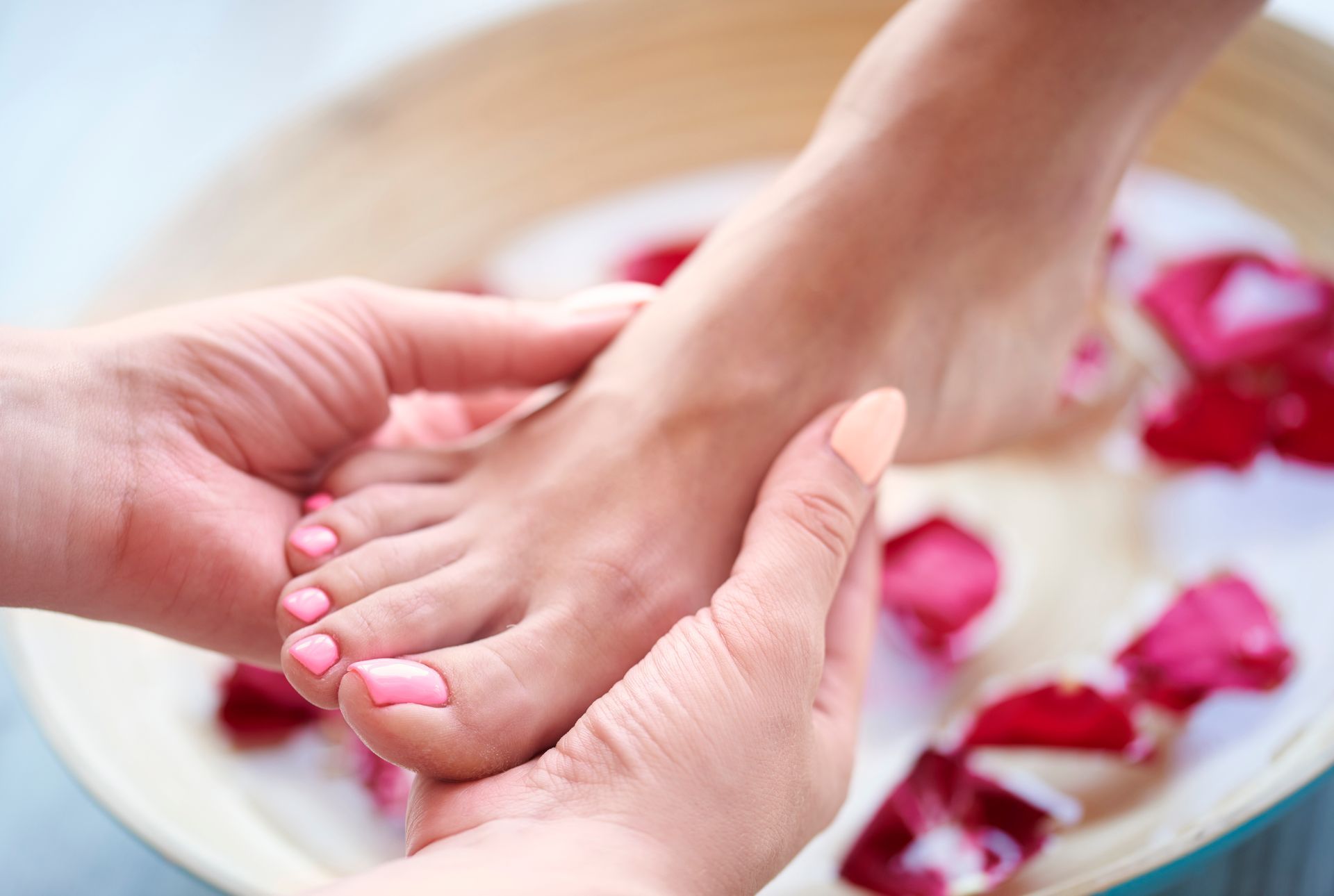 Des mains massent un pied dans un bain de pieds rempli de pétales