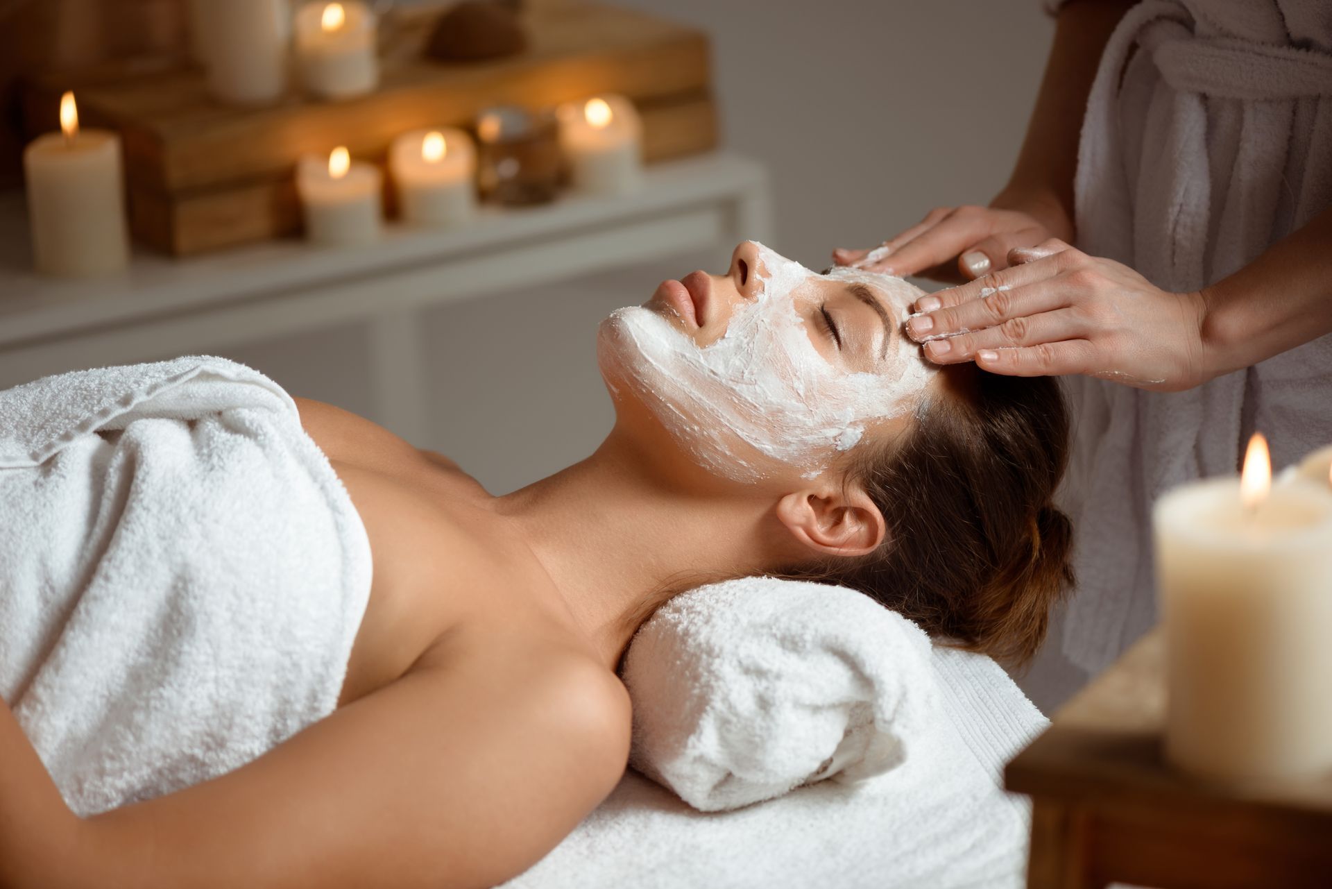 Soin du visage spa : une femme reçoit un masque crème et un massage à la lueur des bougies.