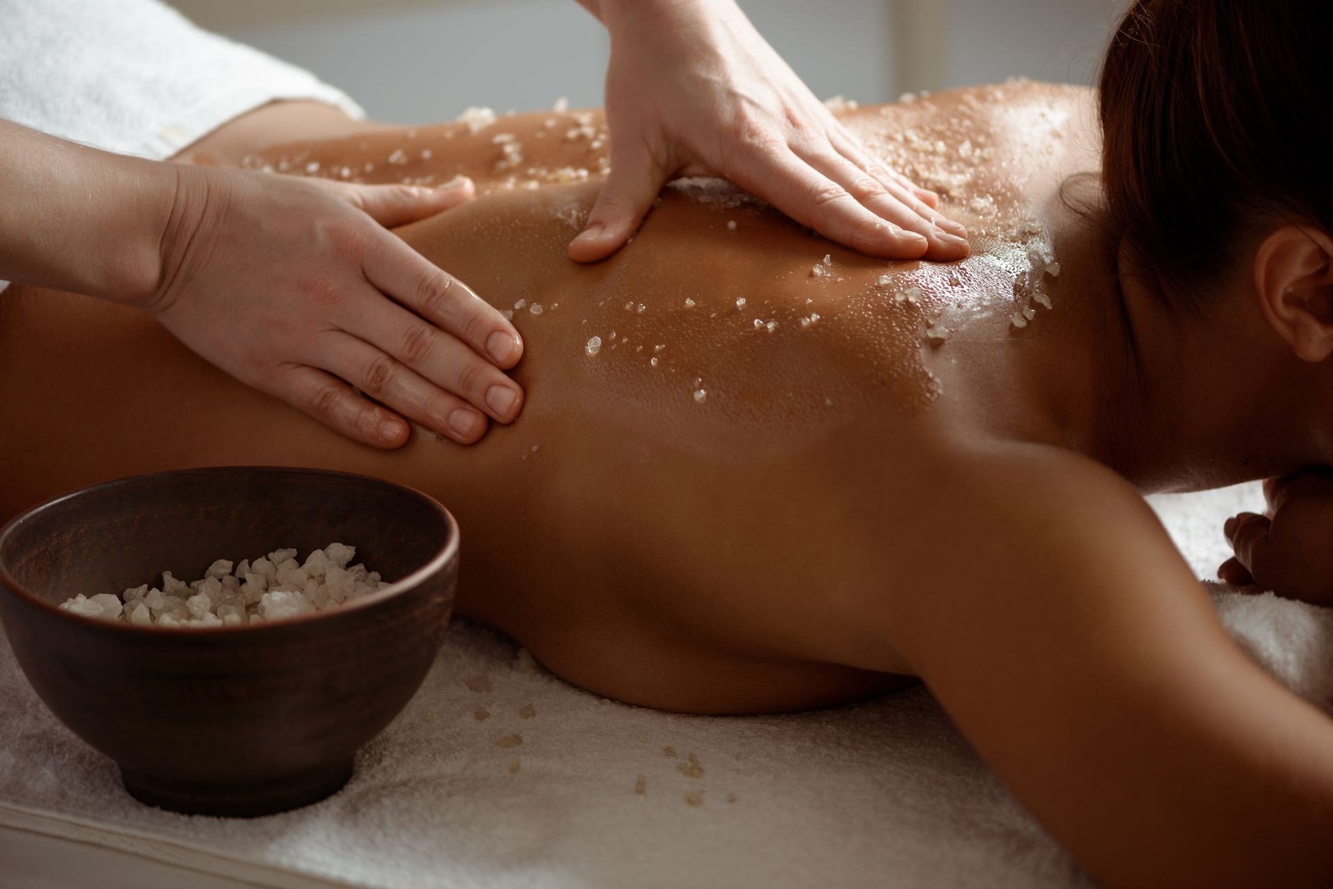Des mains massent un dos luisant d'huile à côté d'un bol de sel dans un cadre de spa