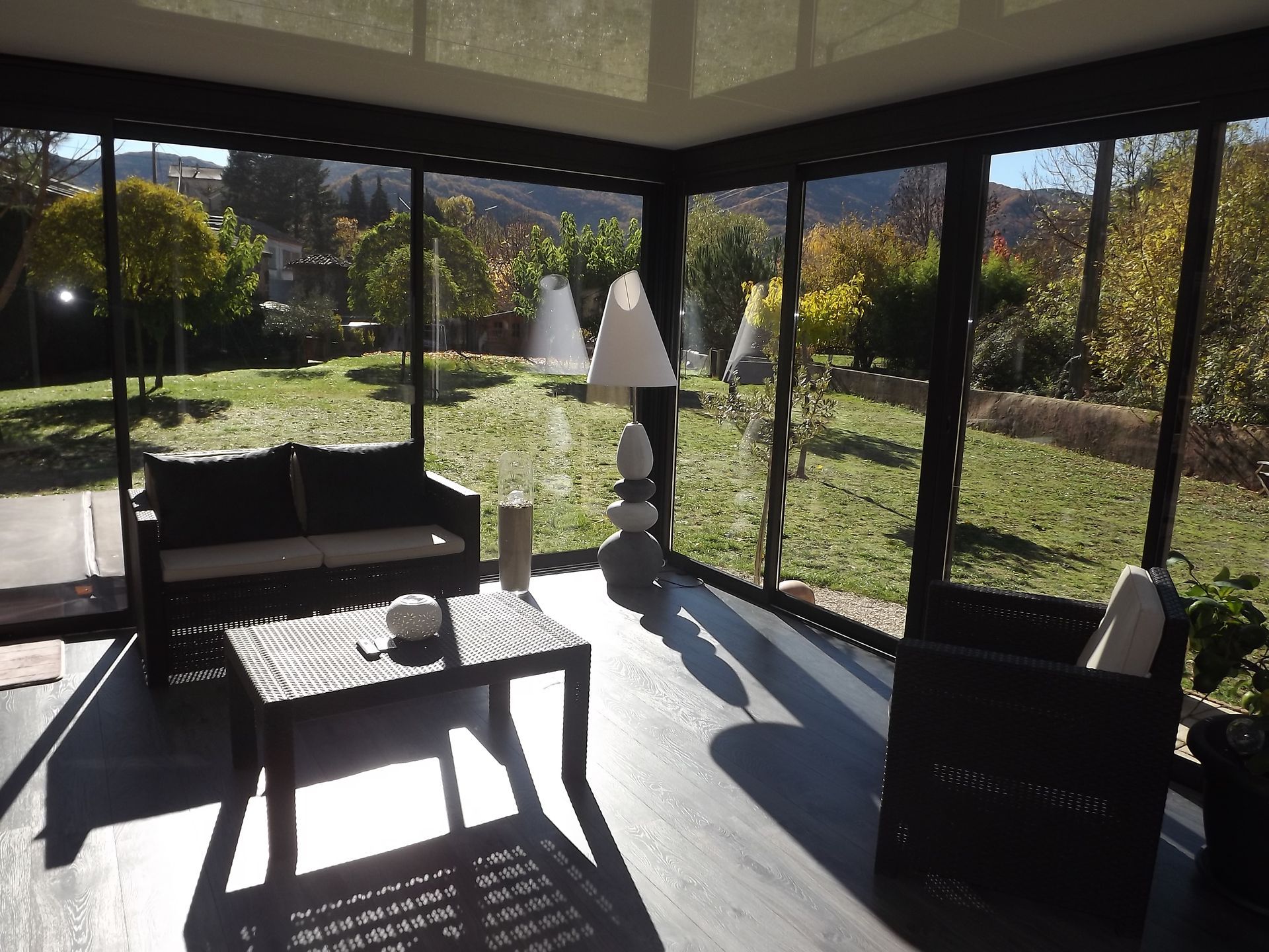 Véranda avec mobilier en osier, donnant sur un jardin verdoyant et arboré.