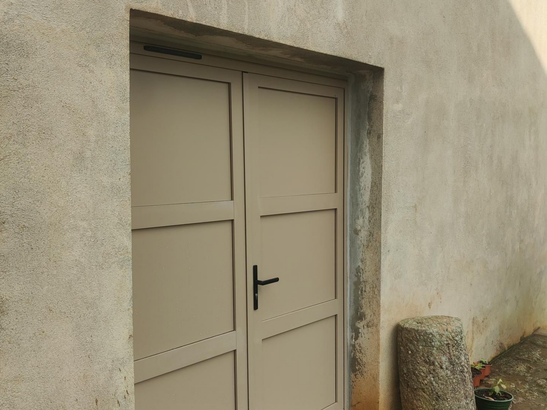 Porte double beige encastrée dans un mur en béton, avec poignée noire à Aubenas.