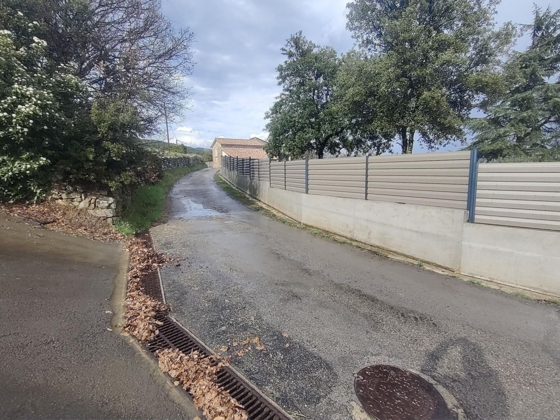 Chantier à Aubenas d'une clôture en béton et d'arbres, ciel couvert.