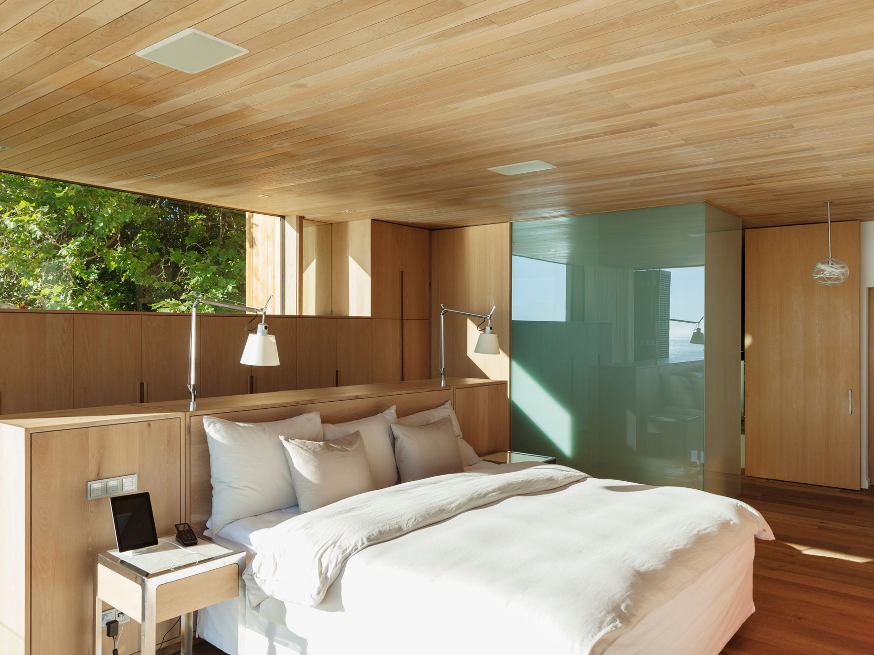 Chambre avec plafond et murs en bois, grand lit avec linge de lit blanc et douche en verre.