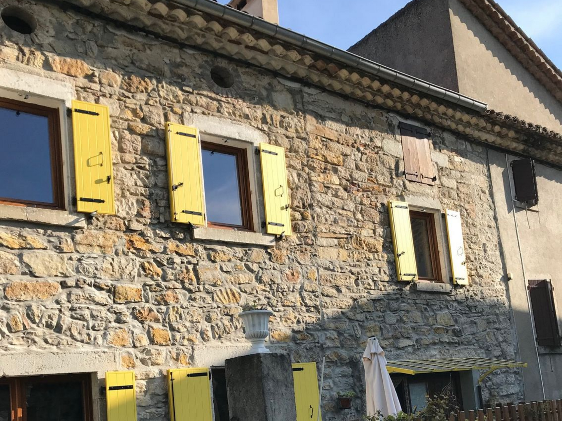 Bâtiment en pierre avec des volets jaunes aux fenêtres.