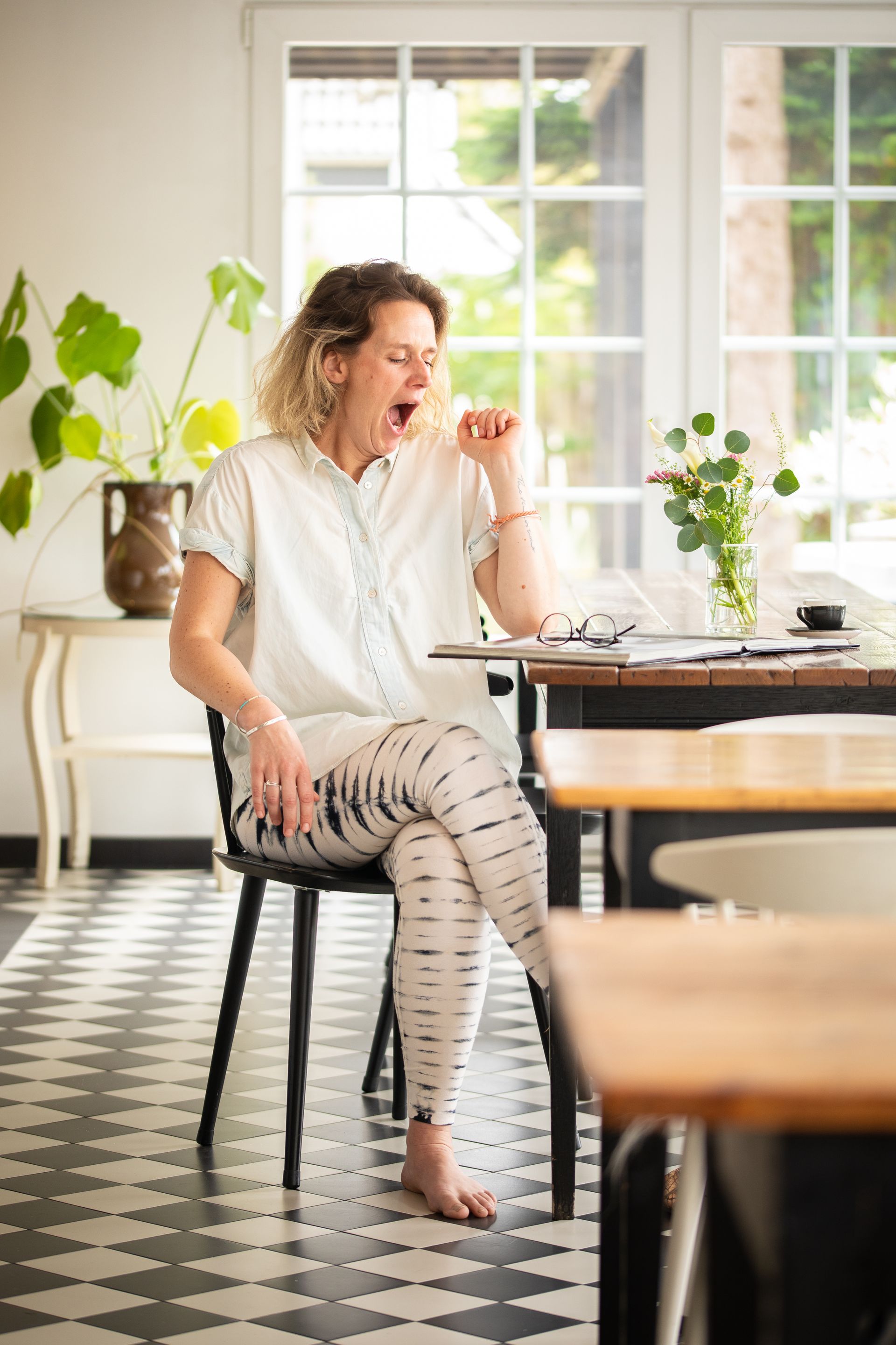Eine Frau gähnt, während sie auf einem Stuhl vor einem Tisch sitzt.