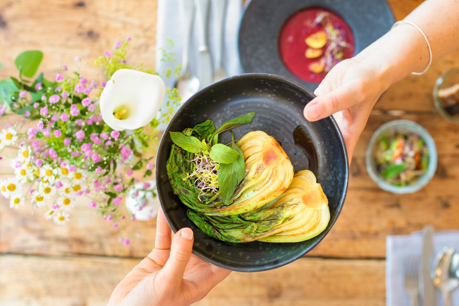 Eine Person hält einen Teller mit Essen auf einem Holztisch.