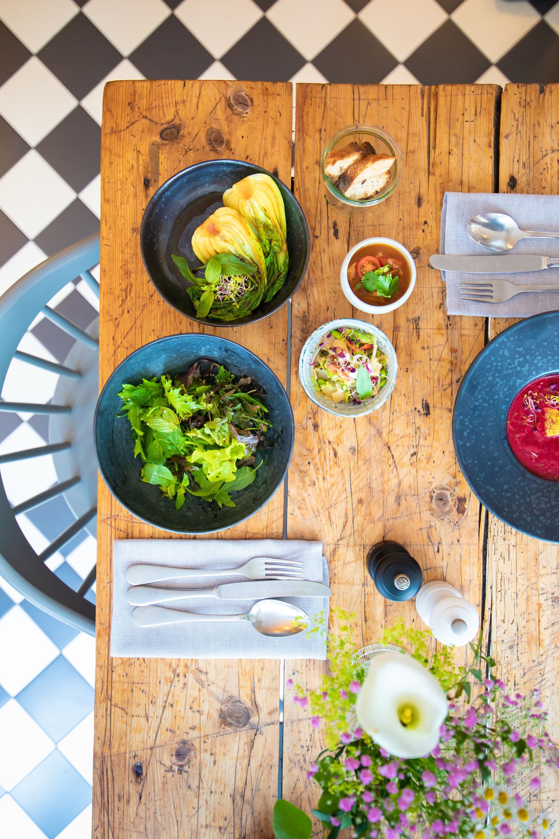 Ein Holztisch mit Schüsseln voller Essen darauf und einem karierten Boden.