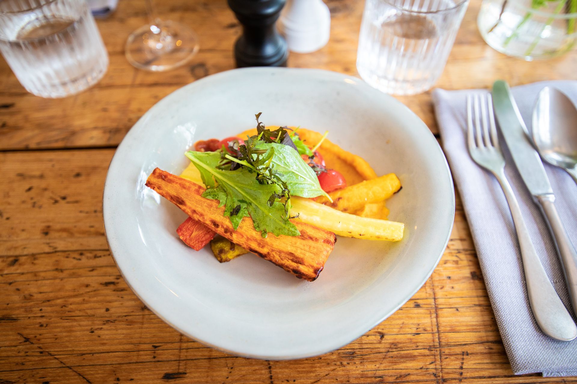 Ein weißer Teller mit Salat und Gemüse auf einem Holztisch.