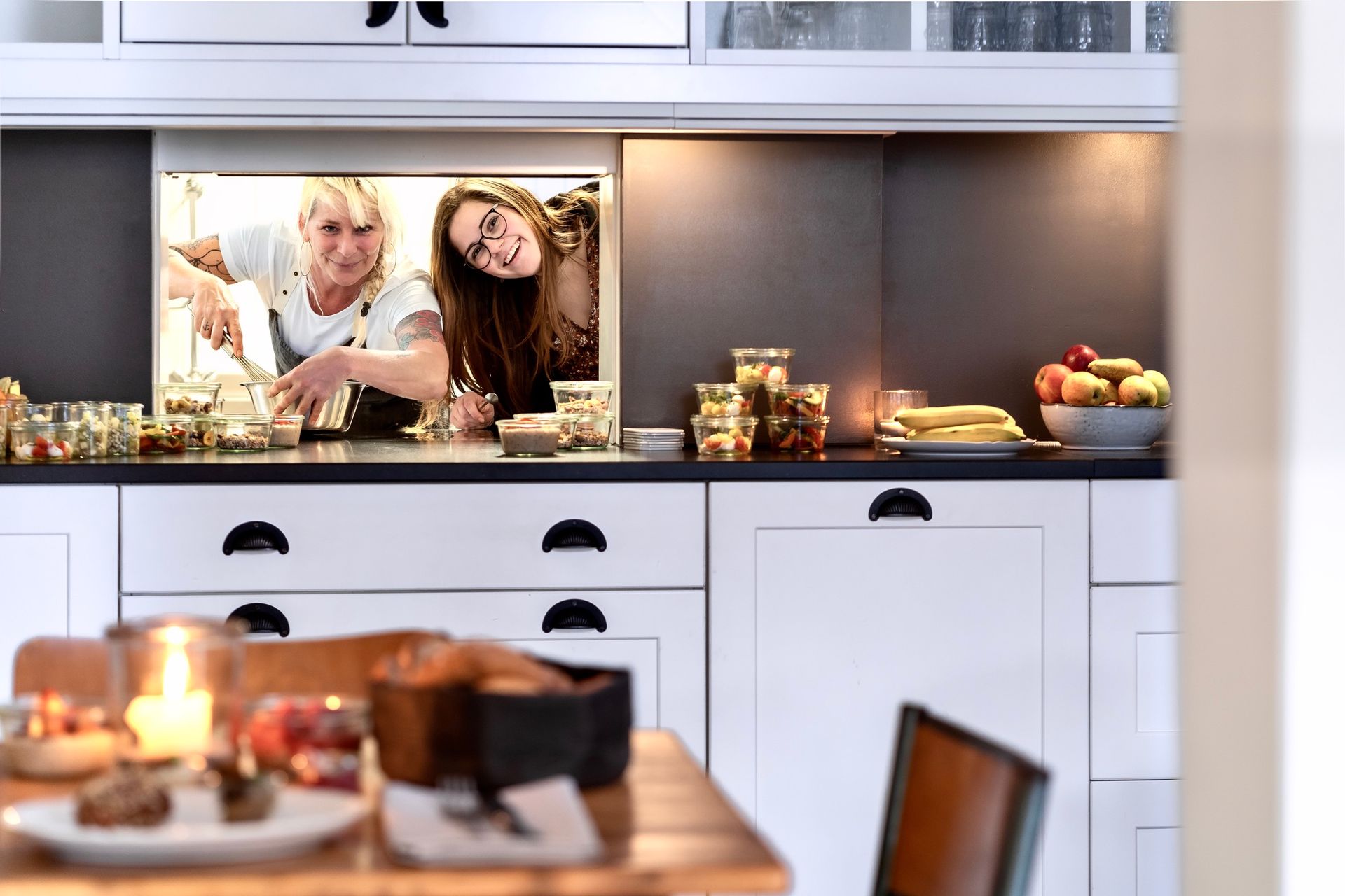 Zwei Frauen kochen in einer Küche. An der Wand hinter ihnen hängt ein Bild von ihnen.