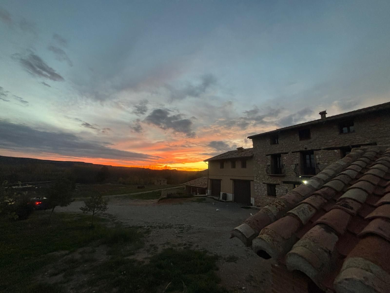 Una puesta de sol sobre una casa con un coche aparcado delante.