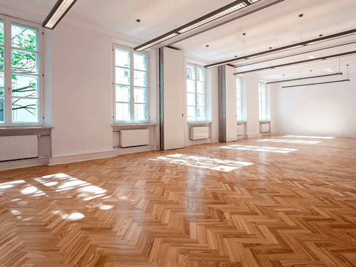 Una habitación vacía con suelo de madera y muchas ventanas.