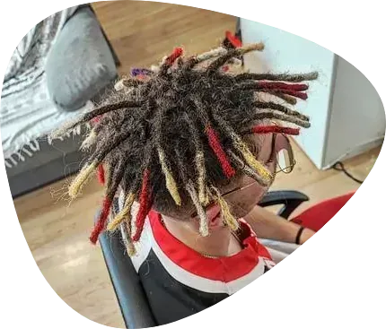 Persona con rastas oscuras y puntas coloridas, sentada en un interior, posiblemente en un entorno hogareño.
