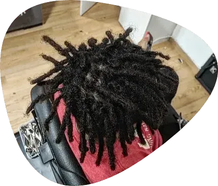 Fotografía cenital de rastas oscuras peinadas en una persona que viste una camisa roja y está sentada en una silla de salón.
