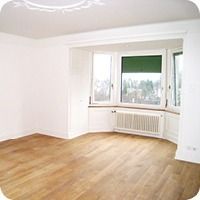 Leeres, weisses Wohnzimmer mit Holzboden, Erkerfenster und Heizkörper unter dem Fenster
