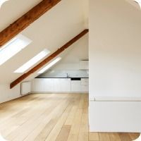 Helles Dachzimmer mit schrägen Holzbalken, Dachfenstern und einer kleinen weissen Küchenzeile.