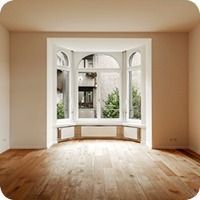 Leerer Raum mit Holzboden und einem grossen Erkerfenster, das natürliches Licht hereinlässt