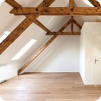 Leeres Dachzimmer mit freiliegenden Holzbalken, Dachfenster, weissen Wänden und hellem Holzboden