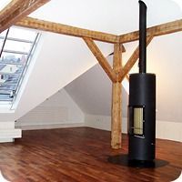 Dachzimmer mit freiliegenden Holzbalken und einem schwarzen Holzofen auf einem Hartholzboden