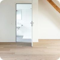 Offene Tür zu einem hellen, weissen Badezimmer in einem minimalistisch eingerichteten Raum mit hellen Holzböden