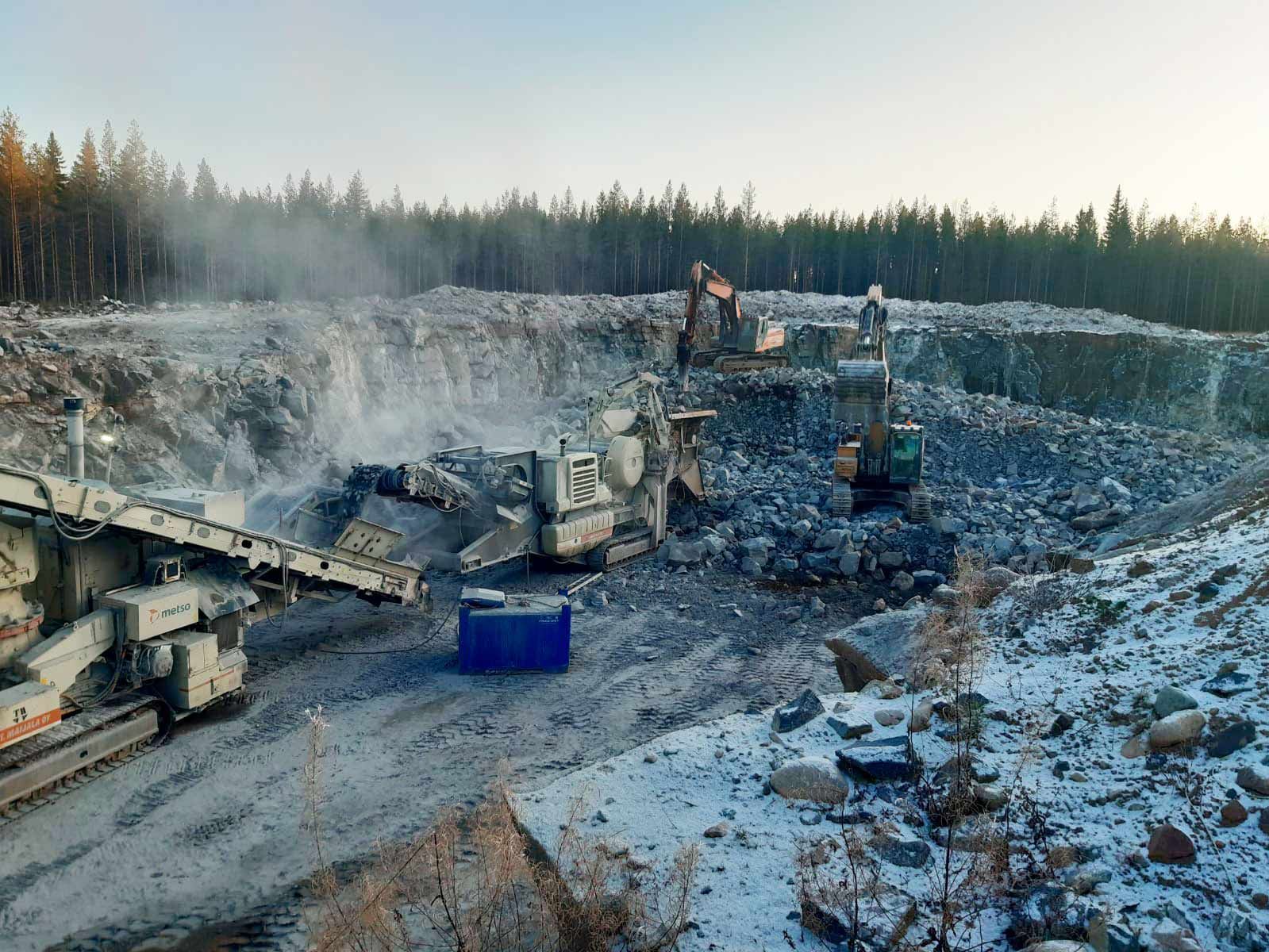 Suuri louhos- tai kaivosalue höyryävine kivimurskeineen, koneineen ja metsäisen horisontin hämärässä