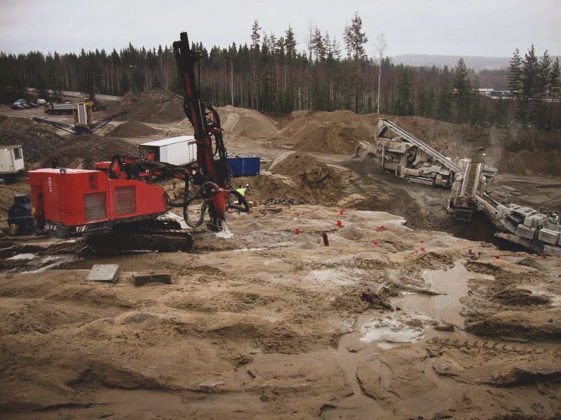 Punainen porauslautta mutaisella kaivosalueella, jossa on sorakasoja ja metsäinen tausta