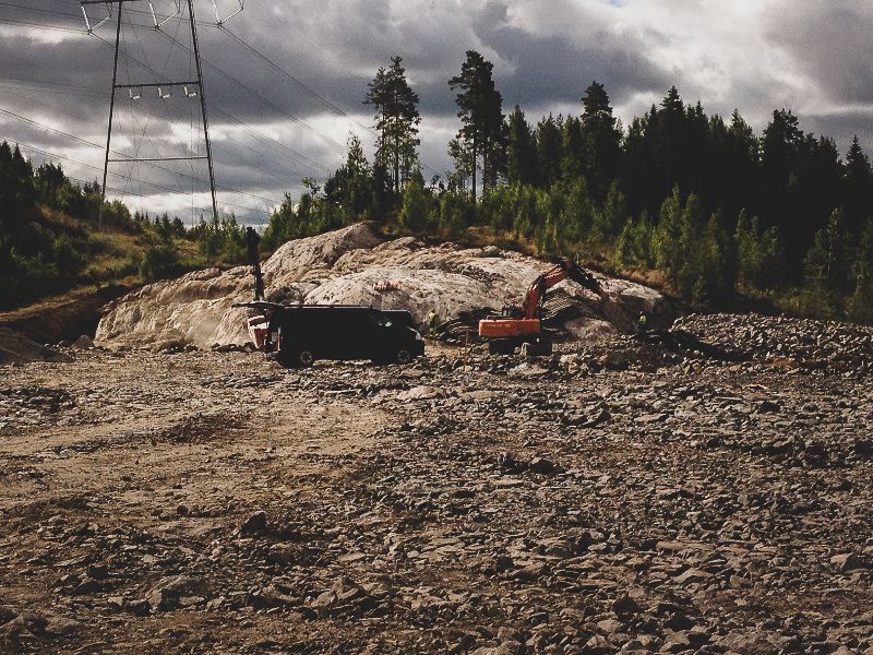 Kivinen raivaus mustalla kuorma-autolla ja punaisella kalustolla metsän lähellä pilvisen taivaan alla