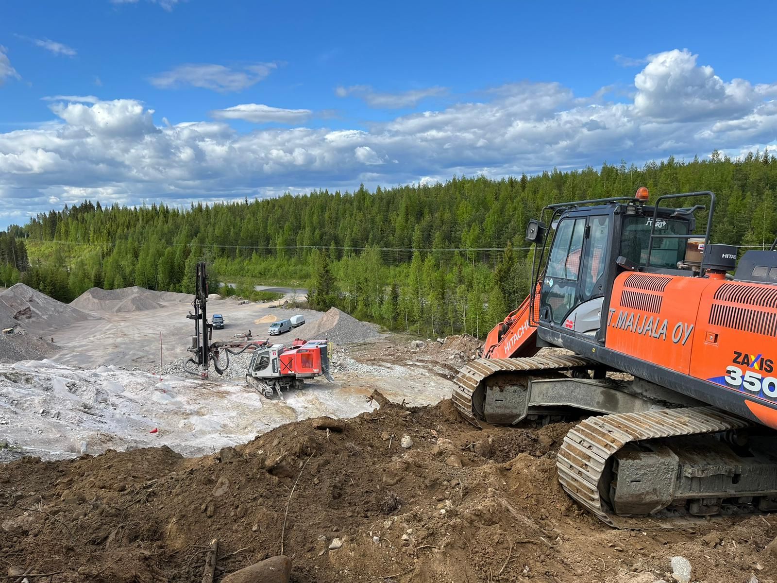 Oranssi kaivinkone mutaisella rakennustyömaalla metsän vieressä sinisen taivaan alla