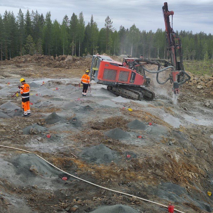 Oranssiin turvavarusteisiin pukeutuneita työntekijöitä punaisen, kaadetun porauslautan lähellä mutaisella rakennustyömaalla