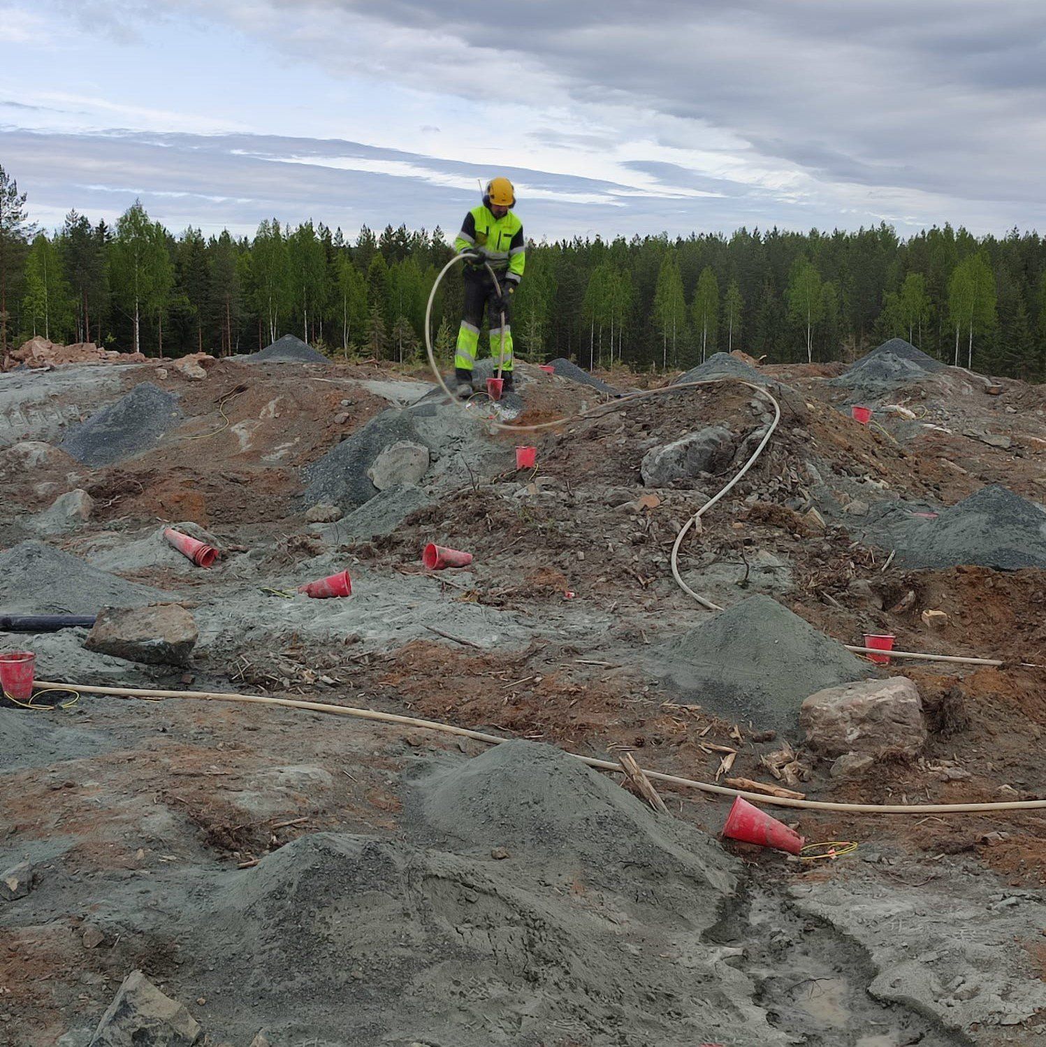 Neonvaloihin pukeutunut turvavarusteisiin pukeutunut työntekijä seisoo kivisellä kaivostyömaalla pilvisen taivaan alla