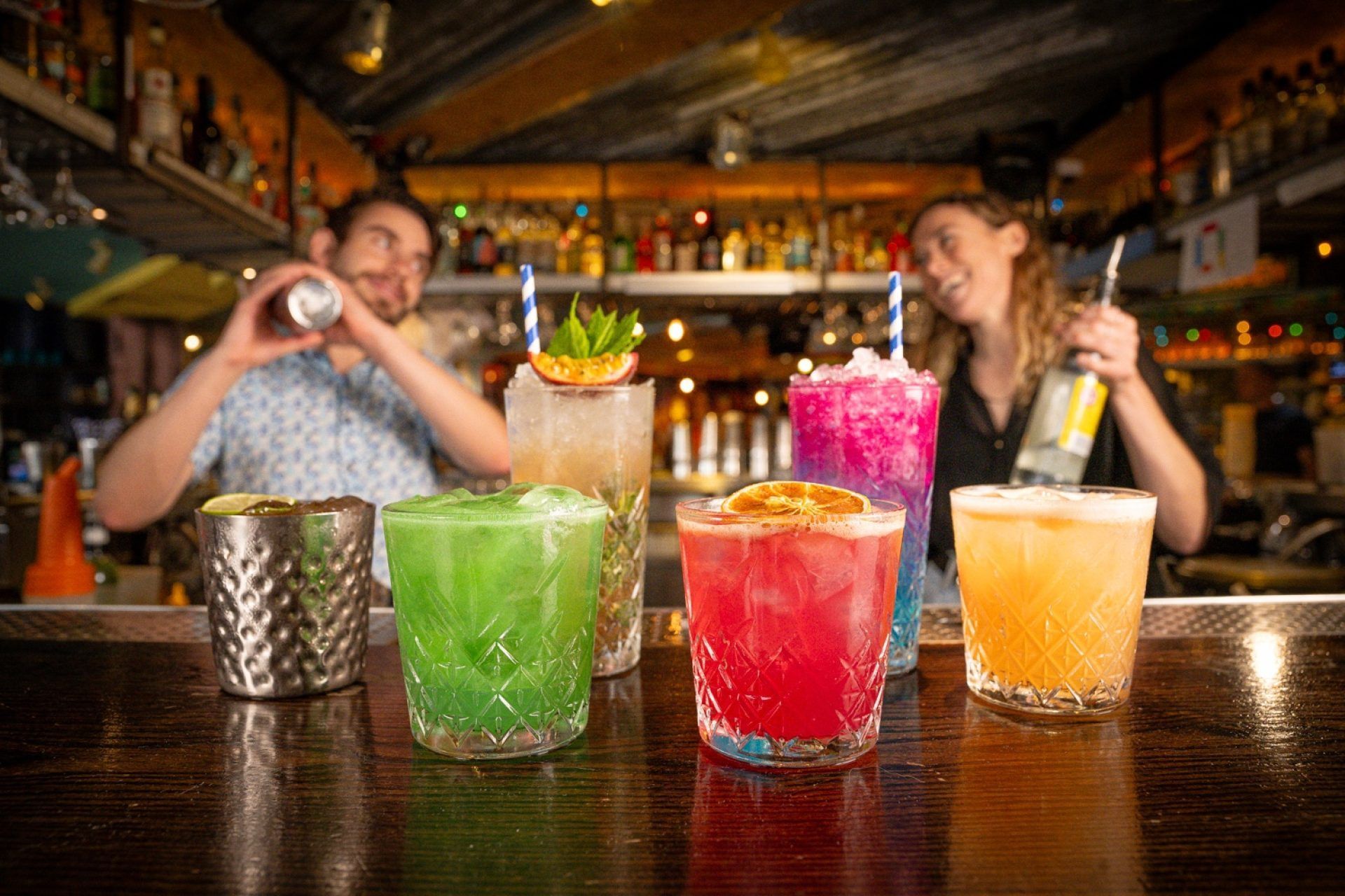 Bar scene with colorful cocktails, bartenders mixing drinks, and bar setting.