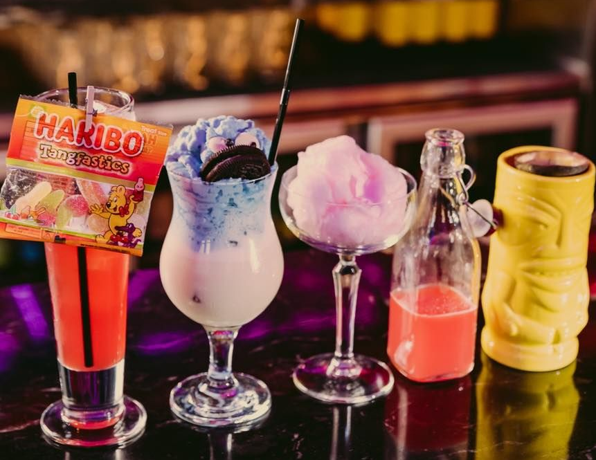 Cocktails on a bar: red, blue, cotton candy, and Tiki mug. Haribo candies attached.