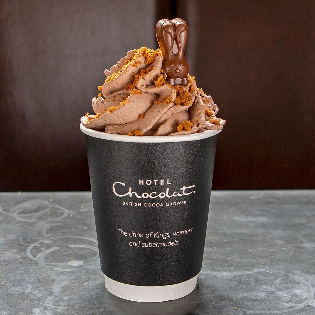 A chocolate drink in a black cup, topped with whipped cream, cookie crumbs, and a chocolate bunny.
