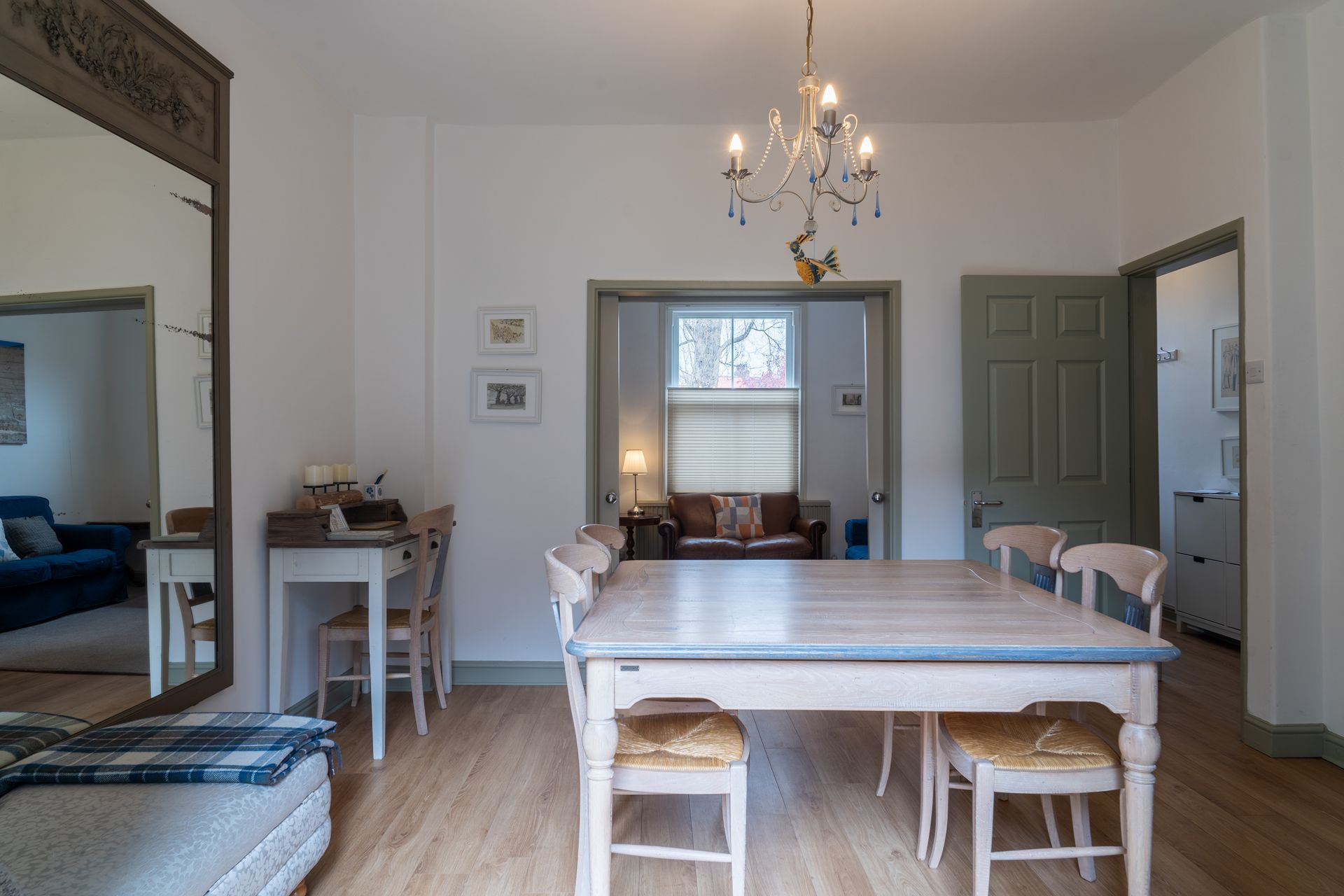 Dining room with a table, chairs, and chandelier. A large mirror reflects a blue couch.