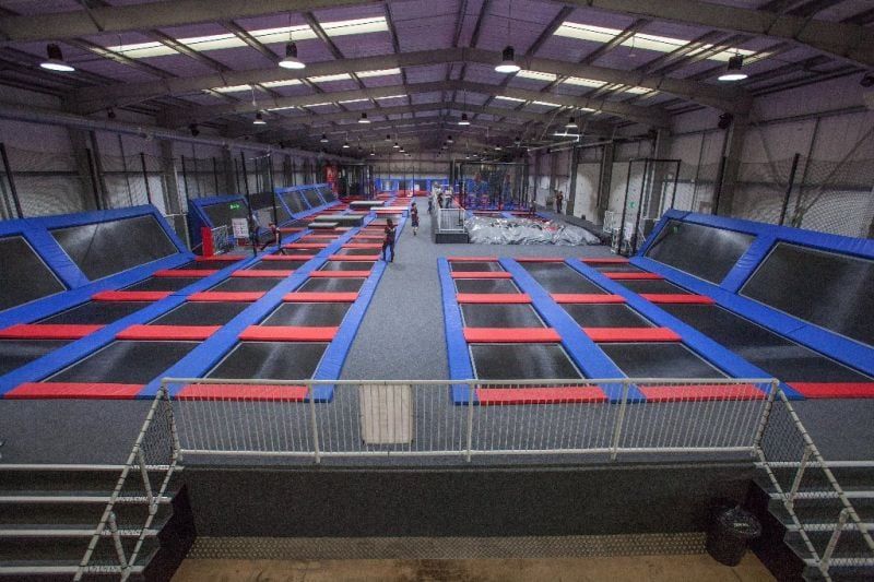 Indoor trampoline park with numerous trampolines, mostly blue and red, under high ceiling.