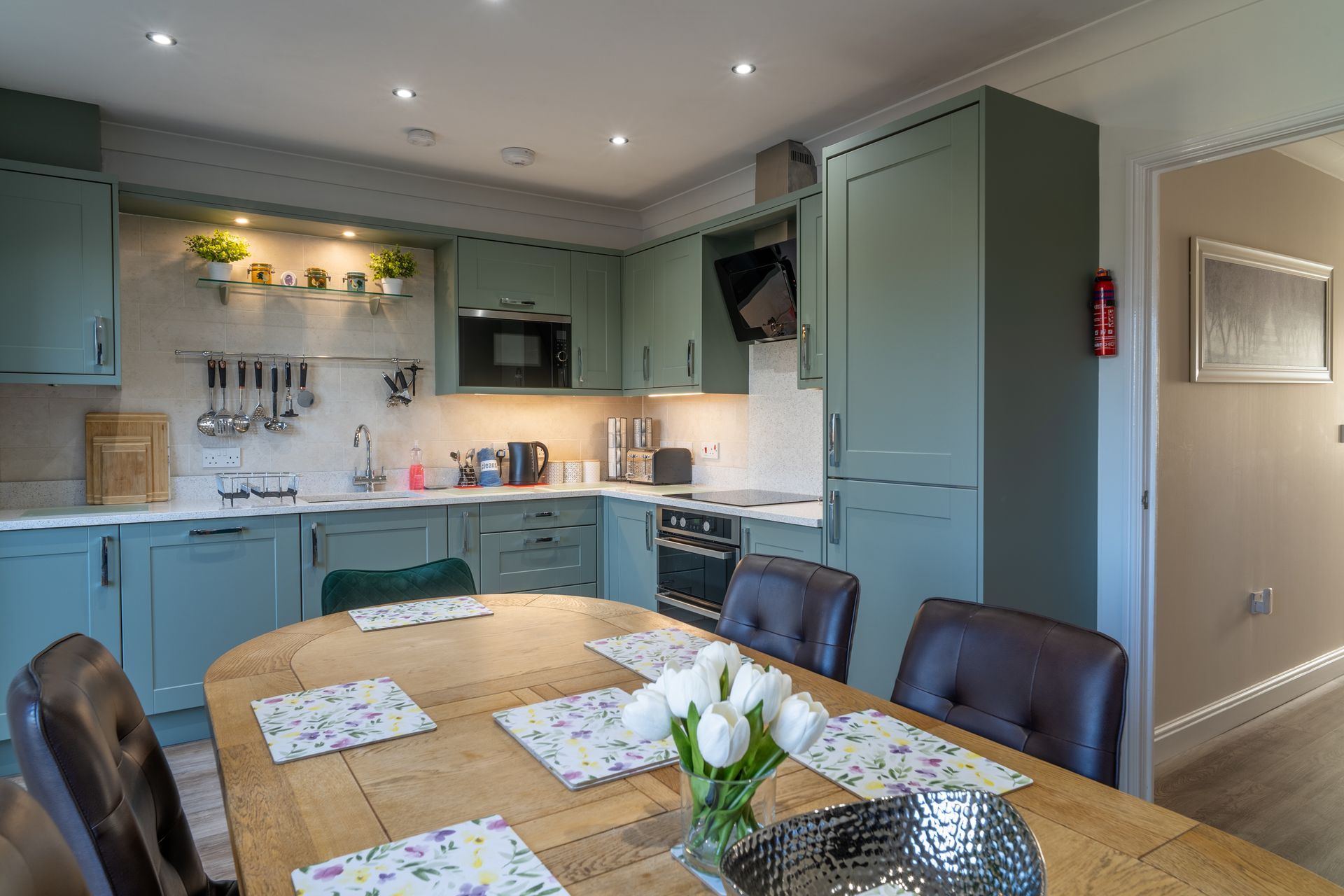 Kitchen with green cabinets, light wood table, and four chairs.