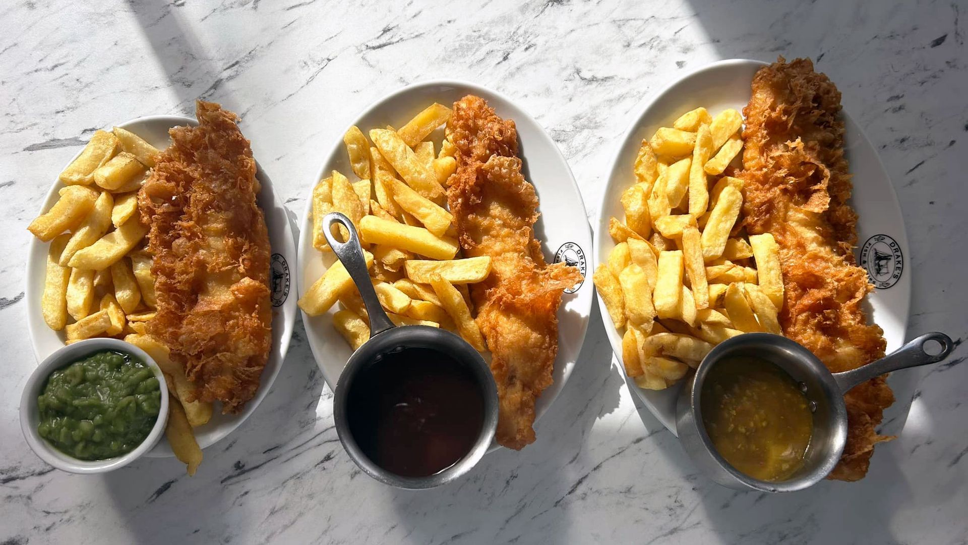 Three plates of fish and chips, each with a dipping sauce.