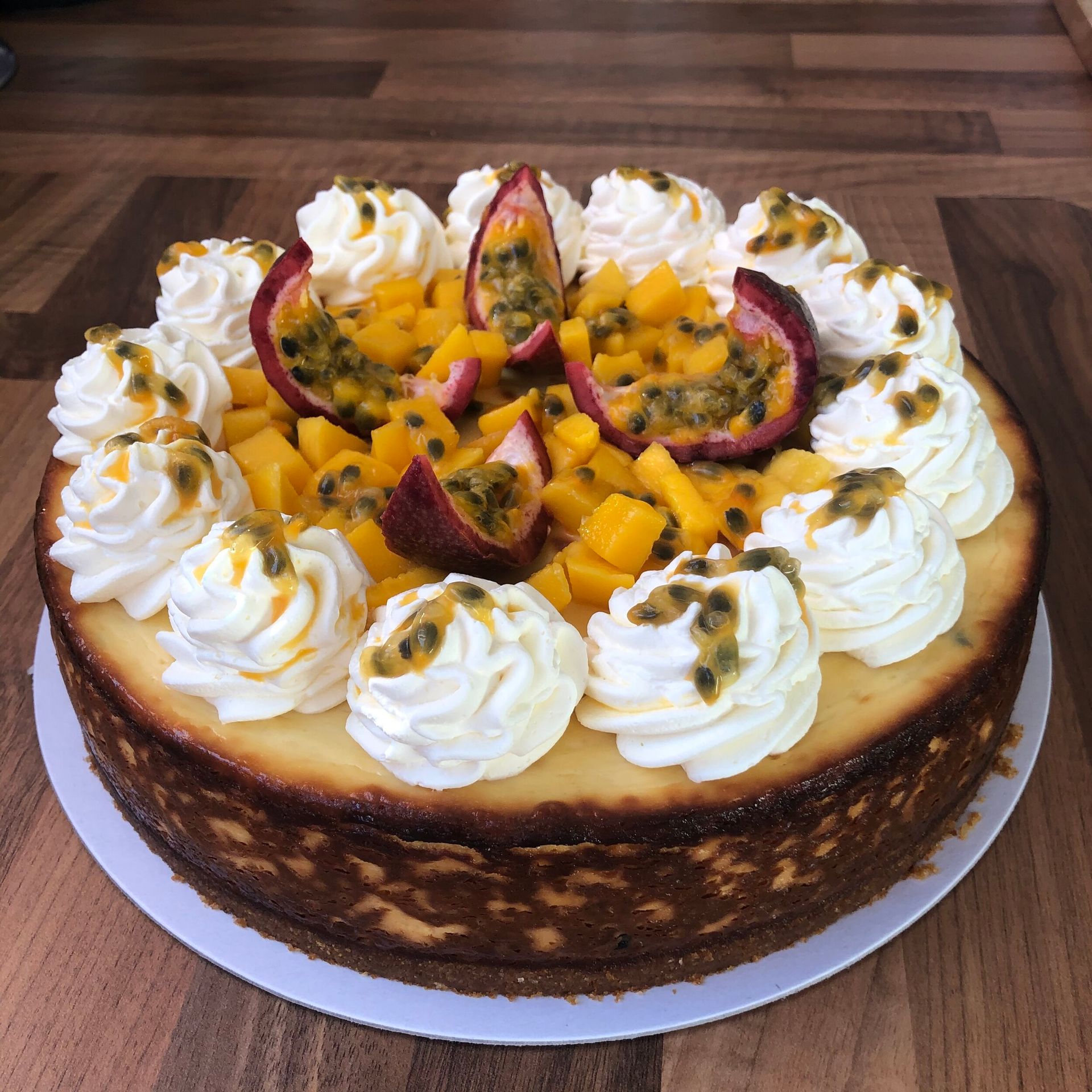 Cheesecake topped with whipped cream, diced mango, and passion fruit on a white plate.